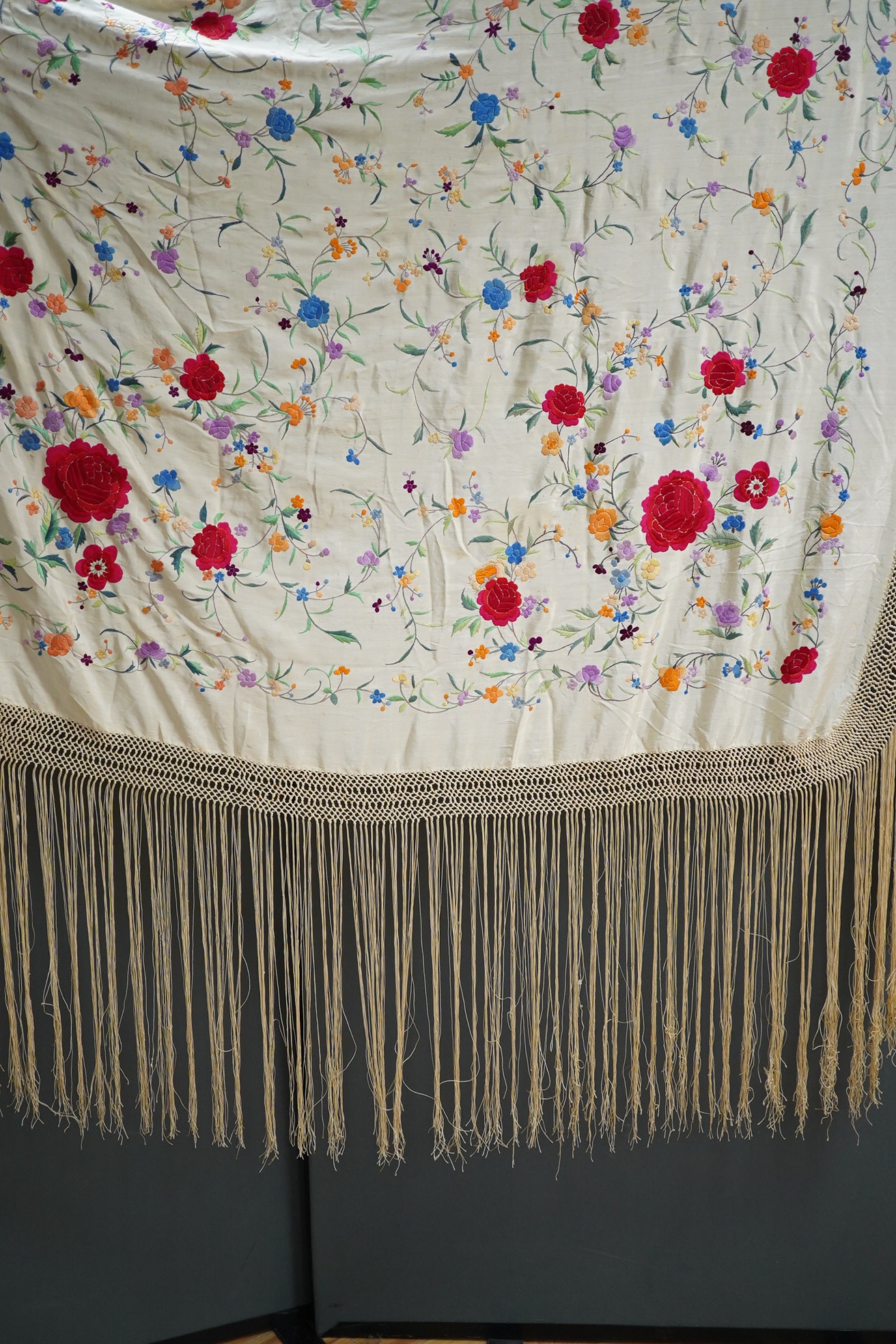 A late 19th / early 20th century Chinese cream silk and polychrome floral embroidered tasselled shawl, embroidered with a rose and floral all over design in a multitude of colours on a plain cream silk background with lo